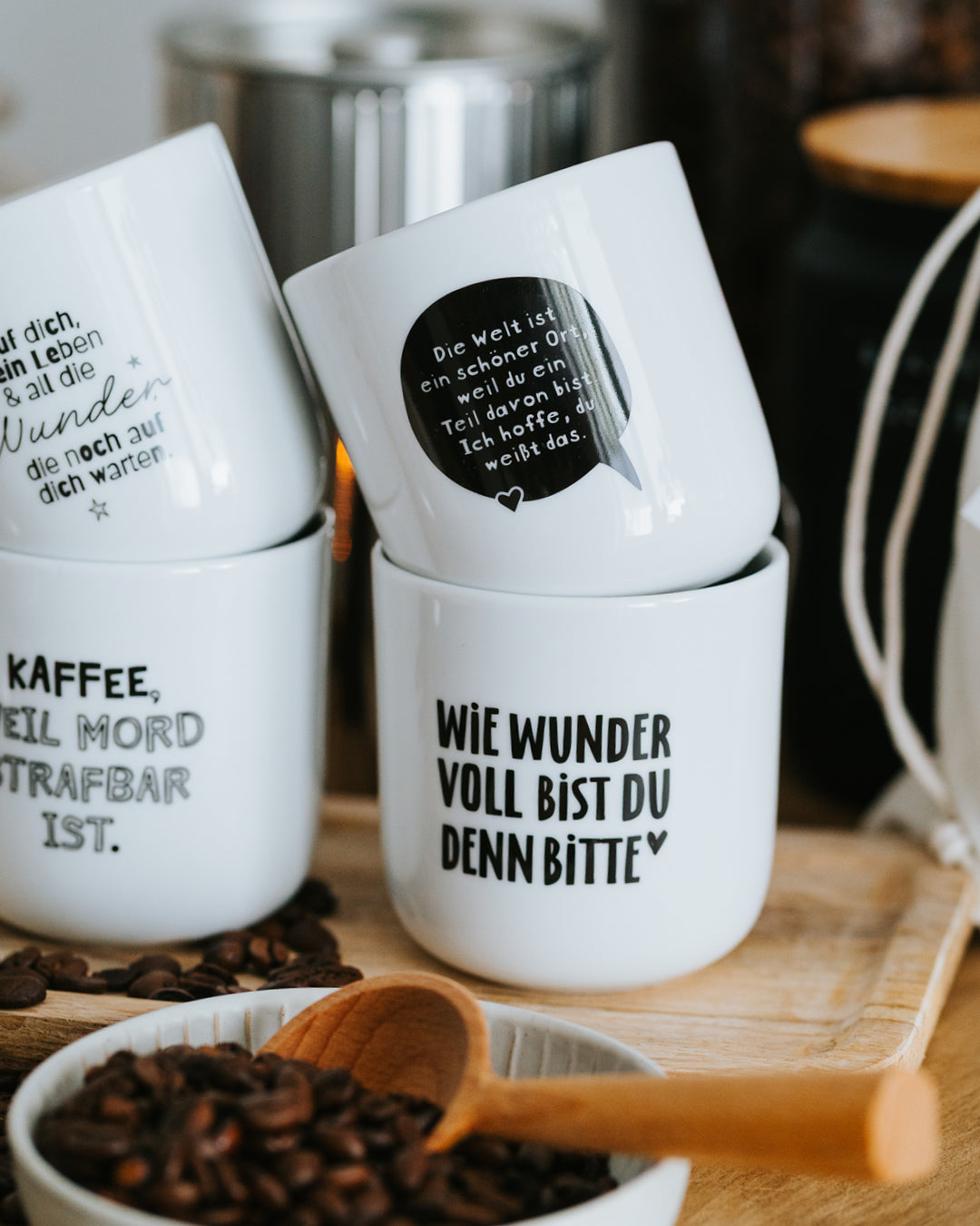 Gestapelte Heldenglück-Porzellanbecher, „Wie wundervoll“ vorne, dazu Kaffeebohnen.