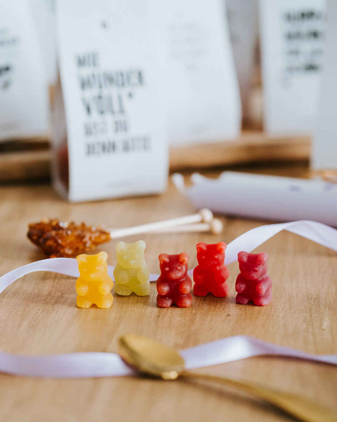 Fünf Fruchtgummi-Bärchen in allen Sorten in einer Reihe, daneben Kandiszucker und Kerze.
