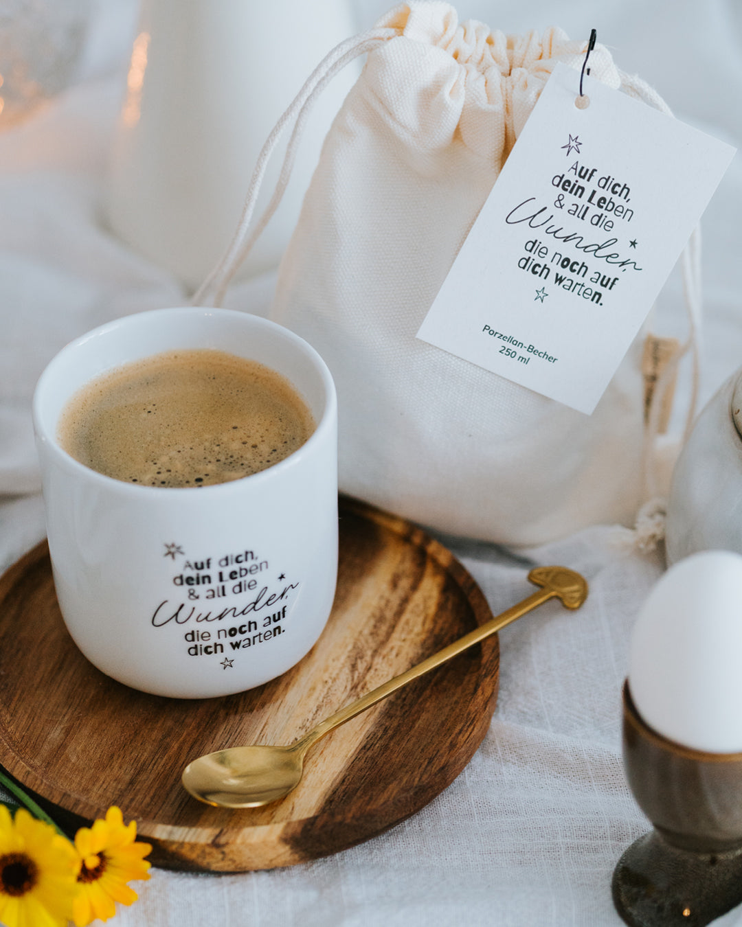 Porzellanbecher „Wunder“ gefüllt mit Kaffee auf Holzteller mit Goldlöffel – ideal für Kaffee oder Tee.