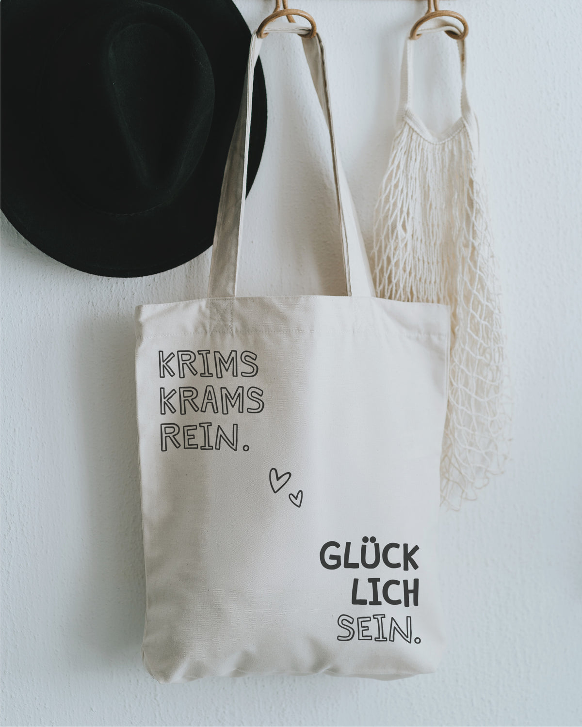Stofftasche natur an der Garderobe mit Hut – „Krims Krams rein. Glücklich sein.“