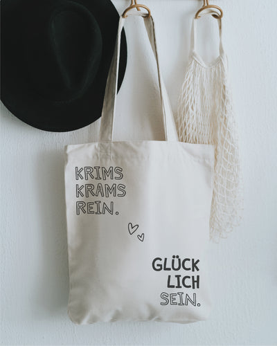 Stofftasche natur an der Garderobe mit Hut – „Krims Krams rein. Glücklich sein.“