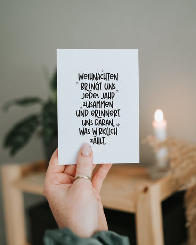 Hand hält die Postkarte „Was wirklich zählt“ vor unscharfen Lichterketten im Hintergrund