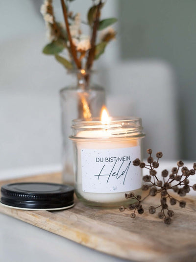 Kerze „Du bist mein Held" im transparenten Glas auf Holzbrett mit Trockenblumen